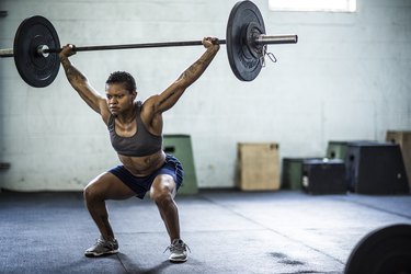 woman doing an overhead barbell squat in the gym as part of a superset workout