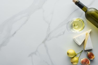 top view of glass of wine, cameembert cheese pieces, figs and pears on white marble tabletop