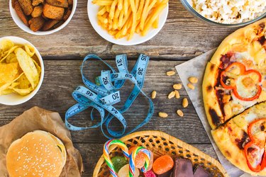 Fast food, tape measure on old wooden background. Concept of junk eating. Toned image. Top view.