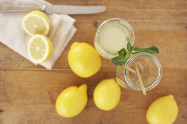 Carafe of lemon juice, sliced and whole lemons on wood, elevated view