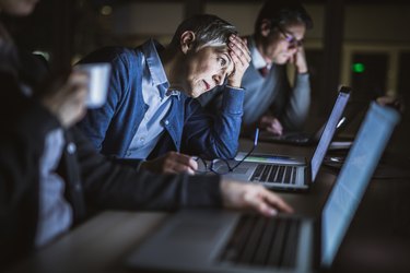 a person looking at a laptop holds their head with a headache