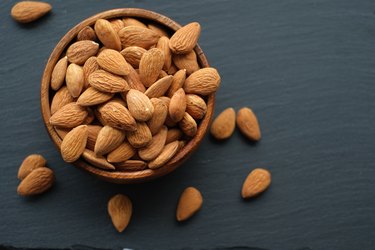 Almonds nut close-up.Raw almonds in a round wooden cup on a black slate background. Nuts in a cup.Vegetarian and vegan food.