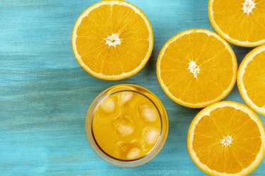 A photo of a glass of fresh orange juice with orange halves, shot from above on a vibrant blue background with a place for text