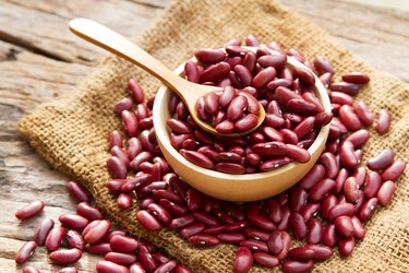 a wooden bowl of red kidney beans with a spoon on a napkin on top of a wooden table