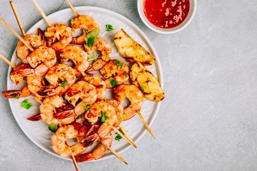 Sweet Chilli Shrimp Skewers with lemon and parsley on gray stone background