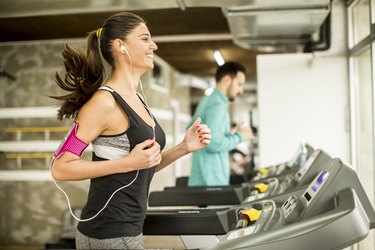 Young woman running on the treadmill and listening to music at the gym