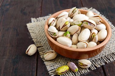 pistachios in a ceramic bowl on a dark wooden background.