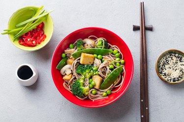 Soba noodles with vegetables and fried tofu in a bowl. Grey background. Top view.