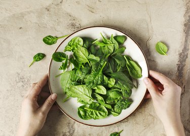 Woman's hands holding a plate with fresh spinach.