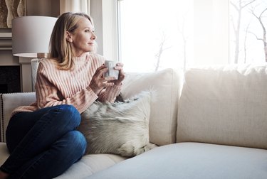 A woman drinking coffee on her couch while looking out the window