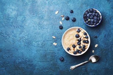 Bowl of oatmeal porridge with banana and blueberry on vintage table top view in flat lay style. Healthy breakfast.