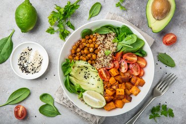 Top view of a bowl of thermic foods, including avocado, quinoa, sweet potato, tomato, spinach and chickpeas