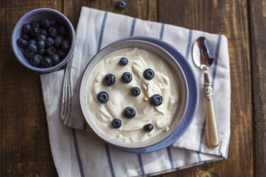 overhead photo of yogurt with blueberries in bowl on wooden table with spoon