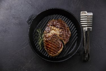 Rib eye steak and tongs on grill pan on dark background