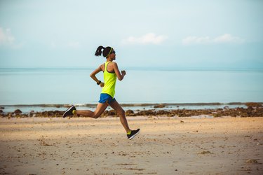 年轻的健身女人在沙滩上跑步