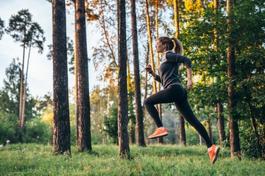 Young female athlete jogging in forest. Jogger doing morning physical training.