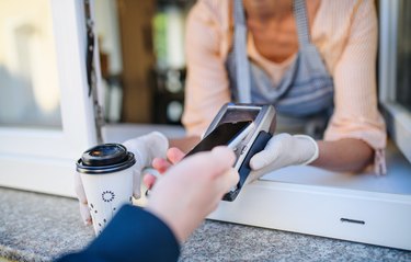 Woman serving coffee through window with contactless payment