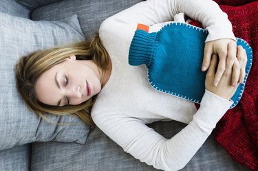 Germany, Bavaria, Munich, Young woman sleeping on couch with hot water bottle