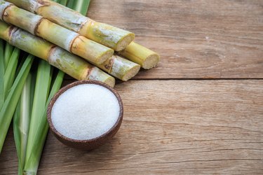 White sugar and sugar cane and leaf on wooden