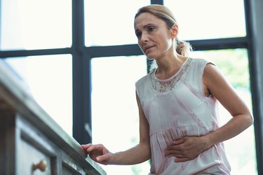 a person holds their stomach in pain after eating holding onto a kitchen counter