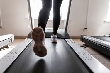 Women's legs run on a treadmill. Young woman engaged in fitness in the gym. Girl in training in the gym. Back view.