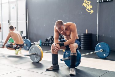 Exhausted man in gym sitting on barbell