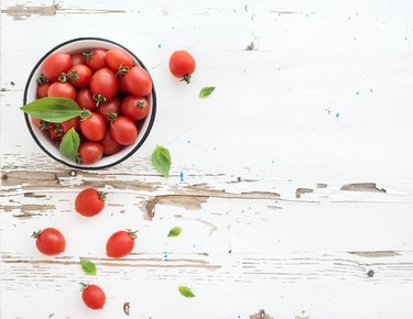 Cherry tomatoes in metal bowl and fresh basil leaves on