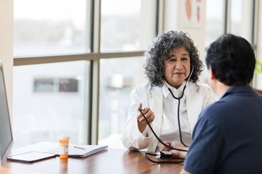 Mature female doctor takes blood pressure of unrecognizable male patient