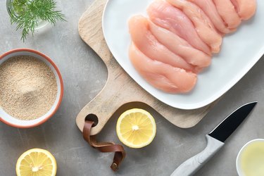 Raw chicken fillet. Meat with breadcrumbs, herbs , lemon and cooking oil. Top view on light