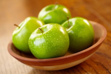 A bowl of green apples on a wooden table
