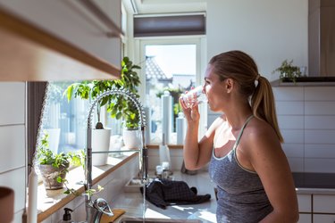 穿运动服的妇女在厨房喝水的侧视图