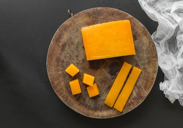 Block, slices and cubes cheddar cheese on a wooden cutting board