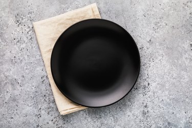 Empty ceramic plate in black with a napkin on a gray concrete table, top view