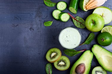 Green smoothie with fruit and vegetable ingredients on grey rustic table with copy space