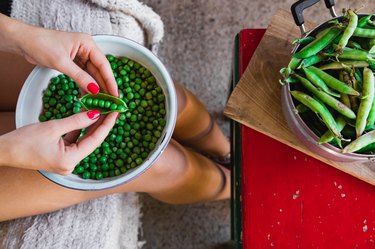 Woman preparing fresh organic peas and taking it out from a shell.