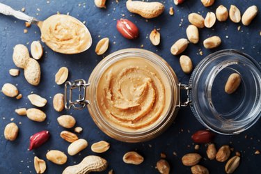 Peanut butter jar and heap of nuts on vintage table top view.