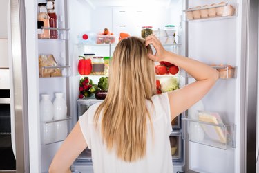 Rear view of a hungry woman looking in the fridge for something to eat