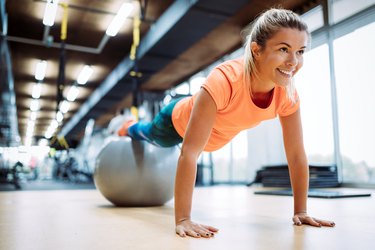 Young attractive woman doing push ups using ball