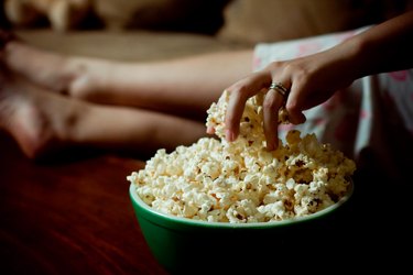 a close-up of a person's hand grabbing a handful of popcorn from a green bowl on their coffee table