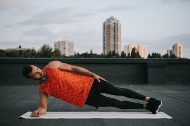 Cyclist doing cross-training strength-training exercise side plank on a rooftop
