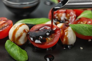 Pouring balsamic vinegar onto fresh vegetable salad on plate, closeup