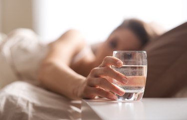 A woman in bed reaching for a glass of water