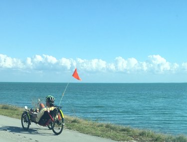 男子在海边的道路上骑着平卧自行车，对着蓝天