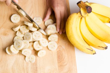 Cropped Hands Cutting Banana On Chopping Board