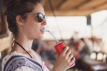 A young woman sitting outside and drinking a red can of soda