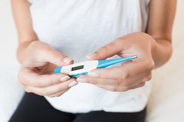 Close up of person holding a blue and white thermometer, measuring their low body temperature