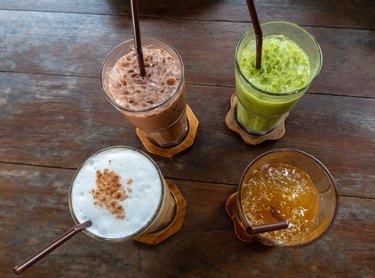 Traditional thai soft drinks on an old rustic wooden table; iced green tea with cream, ice coffee, fruit and herbal drink