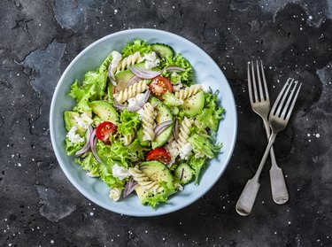 Mediterranean pasta avocado salad on a dark background, top view. Vegetarian diet food concept