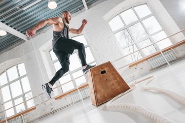 Strong man doing a box jump exercise at workout gym. Male athlete using box for gym exercises
