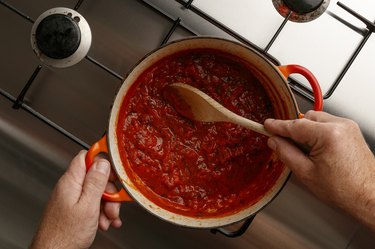 Cooking a traditional gormet tomato sauce and wooden spoon, on a stainless steal hob